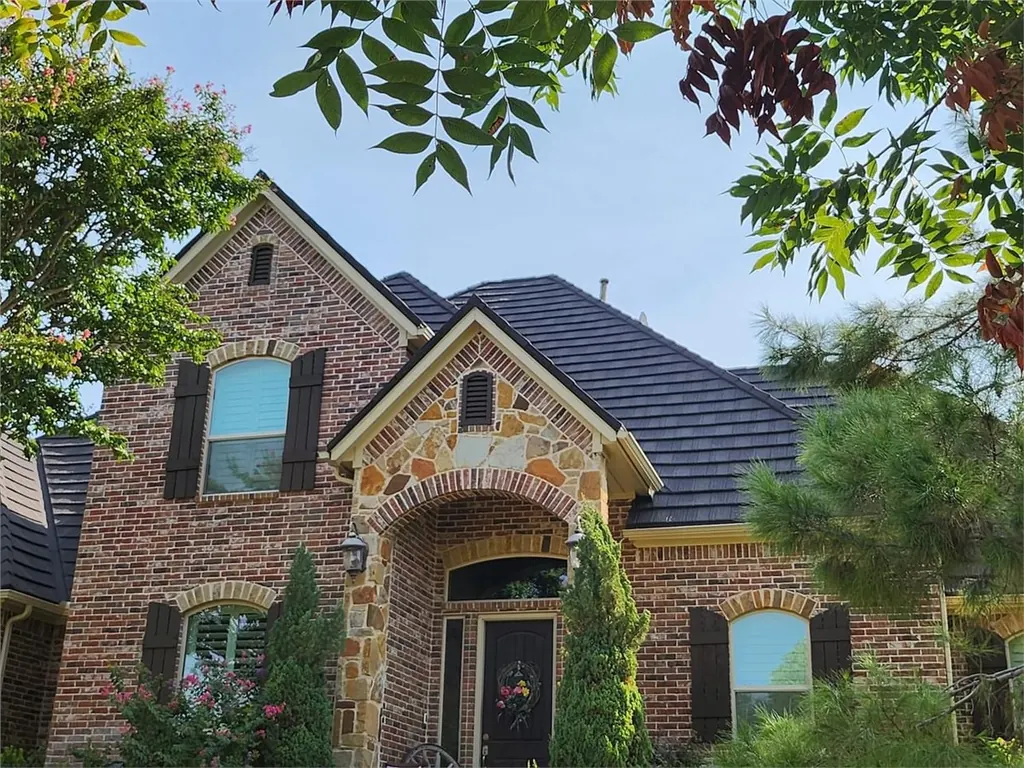 A brick and stone home with a dark steel roof, seen from the front walk.