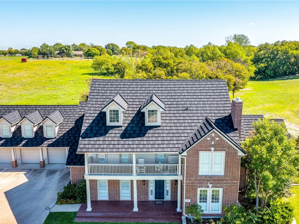 A two-story brick home with a charcoal steel roof that looks like wood shake.