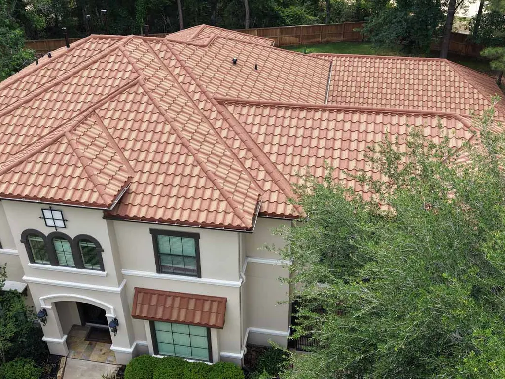A two-story stucco home with a terracotta steel roof that looks like clay tile.